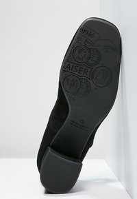 Semelle de chaussure en suède noir avec un talon en caoutchouc texturé et des logos et motifs en relief, incluant le texte "PETER KAISER."