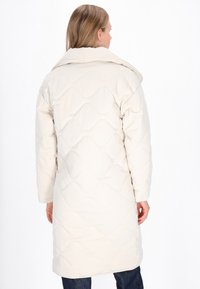 Krémszínű pufferszövet kabát steppelt mintával, nagy gallérral és hosszú ujjakkal, csípő alatt végződik, sima anyagból készült.