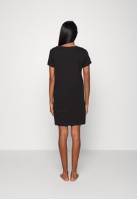 Čierne šaty s krátkym rukávom a voľným strihom, siahajúce po strednú časť stehna, vyrobené z hladkej tkaniny. Jednoduchý dizajn, minimálne detaily na chrbte.