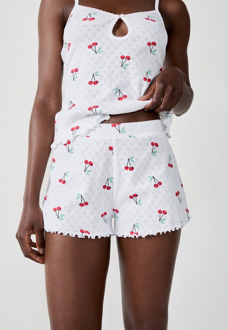 Witte katoenen pyjama set met een mouwloze top en shorts, beide met een rood kersenontwerp en golvende randen. Lichtgewicht, ademende stof.