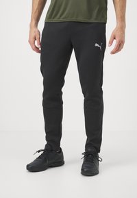 Melnas sporta bikses no mīksta auduma ar šauru piegriezumu, sānu kabatām un sudraba Puma logo kreisajā augšstilbā.