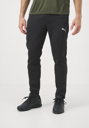Pantalones atléticos negros hechos de una tela suave, con un corte ajustado, bolsillos laterales y un logo plateado de Puma en el muslo izquierdo.