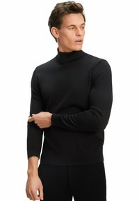 Schwarzer Rollkragenpullover mit langen Ärmeln und gerippten Bündchen, der ein strukturiertes Strickdesign aufweist. Figurbetonte Silhouette. Getragen über dunklen Hosen.