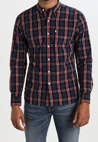 Camicia button-up in pattern scozzese navy, rosso e bianco. Maniche lunghe, colletto standard e dettaglio tasca sul petto. Materiale in misto cotone.