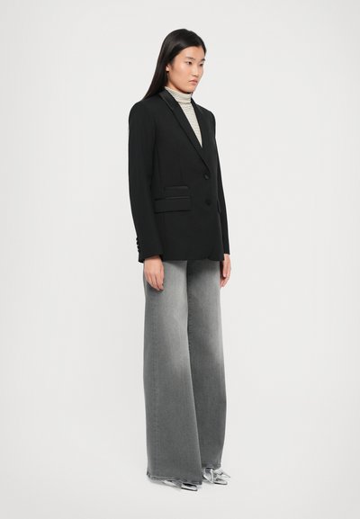 Black tailored blazer with two front pockets and a structured design, paired with wide-leg gray denim jeans and silver-accented shoes.