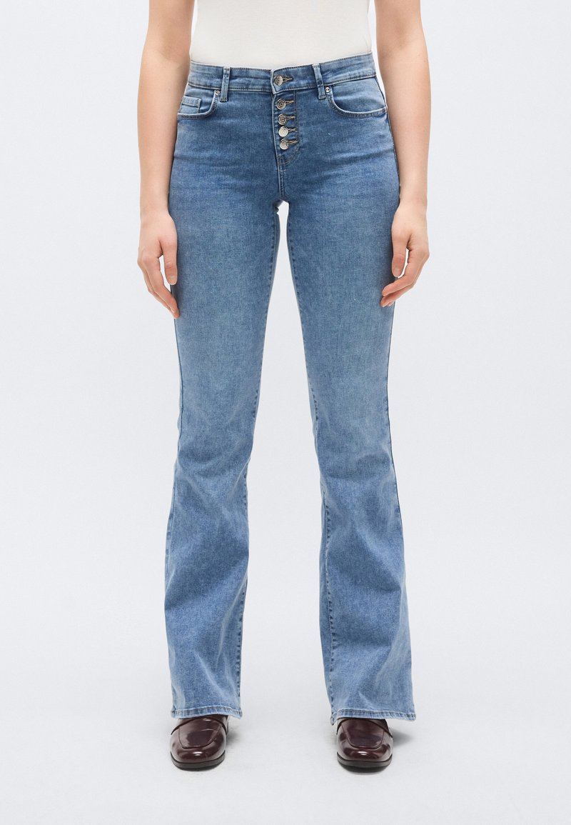 Világoskék farmerből készült, magas derekú, bőszárú farmernadrág öt gombos záródással, elülső zsebekkel és finom varrási részletekkel. Sima tapintású felület.