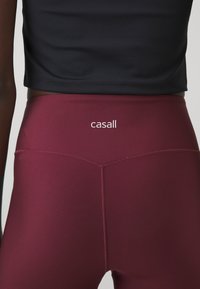Bordové legíny s vysokým pásom, s názvom značky "casall" v bielej farbe, navrhnuté z hladkého, elastického materiálu a s minimálnymi švami.