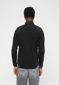 Mustad pikkade varrukatega särk terava krae, nööbitavate mansettide ja õrna seljaosa detailiga. Kangas tundub siledana, kerge läikega.