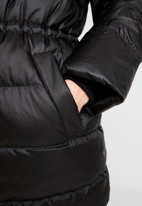 Chaquetón negro con un acabado texturizado. Presenta una cintura ceñida, puños anchos y un bolsillo lateral. Material suave y ligero.