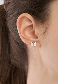Orecchini a stud a forma di farfalla realizzati in metallo con una finitura in smalto bianco, caratterizzati da piccoli strass al centro.