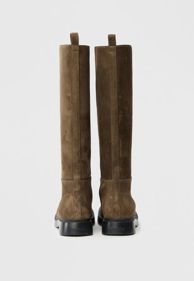Καφέ σουέντ μπότες μέχρι το γόνατο με ομαλή υφή, ορθογώνιο σχήμα και μαύρη λαστιχένια σόλα. Διαθέτουν δύο θηλιές στην κορυφή.