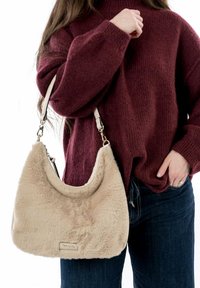 Sac à épaule en fausse fourrure beige avec une bandoulière blanche réglable et des fournitures en argent, présentant une forme arrondie et une texture douce.