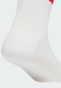 Bela športna nogavica z rebrasto teksturo, ojačanim peto in rdečim poudarkom na vrhu. Klasična zasnova za dodatno udobje.