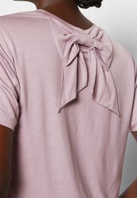 T-shirt rose clair avec un détail nœud au niveau de l'encolure arrière. Confectionné en tissu doux avec une coupe décontractée. Manches courtes et texture lisse.