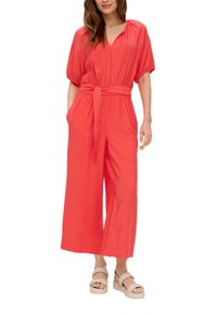 Koraalkleurige jumpsuit met een V-hals, korte pofmouwen, striktaille en brede pijpen. Gemaakt van lichte stof met een gestructureerde afwerking.