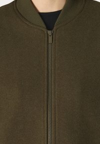 Olive green bomber jacket with a textured, soft finish. Features a central zipper, ribbed collar, and no visible markings or designs.
