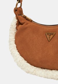 Borsa a tracolla in suede marrone con un bordo di pelliccia bianca e soffice. Presenta un logo a triangolo dorato e una chiusura con zip. Forma rotonda con una sola tracolla.