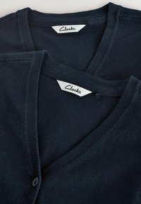 Marinblåa koftor staplade, med v-ringningar, enkel knappstängning och "Clarks"-etiketter. Mjuk stickad textur med subtil lyster.