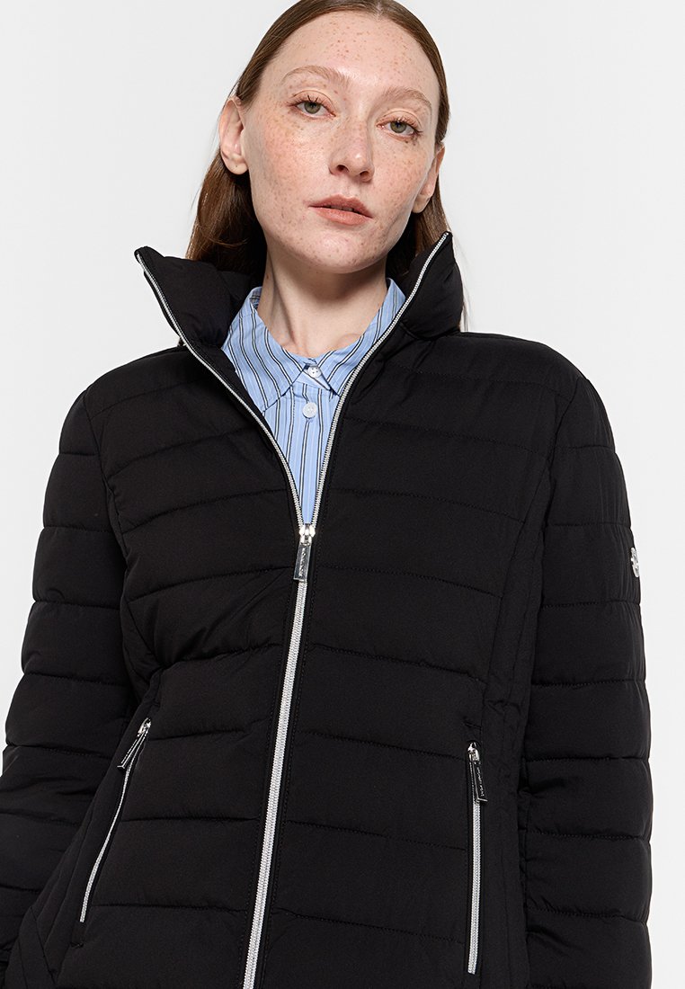 Giacca a vento nera con colletto alto, chiusura con zip frontale e texture trapuntata orizzontale. Presenta dettagli in metallo argentato e tasche laterali.