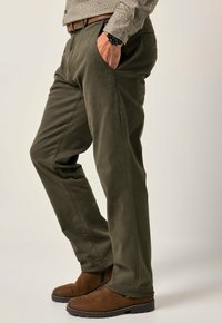 Olivgrüne Baumwollhose mit seitlichen Taschen, geradem Schnitt und glatter Textur. Getragen mit braunen Knöchelstiefeln.