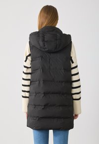 Schwarze Pufferweste mit Kapuze, ausgestattet mit einem gesteppten Design und ribbed Strickärmel in Creme- und schwarzem Streifenmuster.