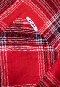 Tissu à carreaux rouge avec un motif à damiers comprenant différentes teintes de rouge, noir et blanc. Une étiquette blanche avec "GARCIA" est visible.