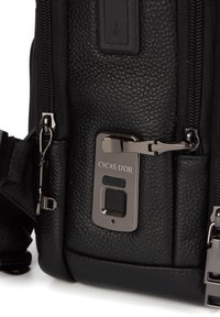 Musta teksturoitu nahkalaukku, jossa on metallinen suljin, brändilogo ja USB-portti. Vetoketjuyksityiskohdat ovat näkyvissä sivuilla.