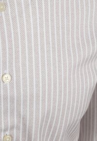 Lichtgekleurde shirt met dunne verticale strepen in beige en wit, met een gestructureerde afwerking en een klein, rond knoopdetail.