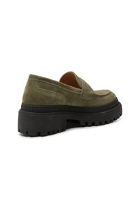 Maslinasto zelene suede mokasine s crnom debelom gumom i dekorativnim šavovima. Imaju zaobljen vrh i nisku kroja za lako obuvanje.