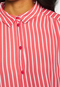 Red and white striped blouse with a pointed collar, featuring matching buttons down the front and a soft, textured fabric.