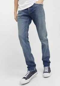 Jeans en denim bleu clair avec une coupe droite, présentant des nuances légères, des poches standards et une finition légèrement délavée, portés avec des baskets navy.