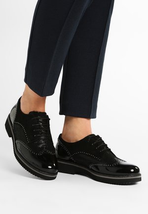 Zapatos de cuero negro con acabado brillante en charol y acentos de ante. Presentan un diseño de cordones en la parte delantera, detalles de brogue y suela de goma texturizada.