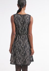 Robe en dentelle noire avec un motif floral, longueur au genou, silhouette sans manches, et taille cintrée. Tissu doux et texturé.