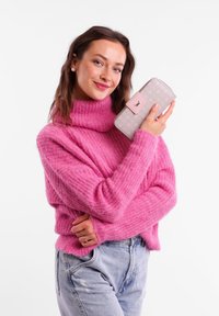 Pink knitted sweater with a high neckline, paired with light blue denim jeans. Holding a light pink wallet with subtle floral patterns.