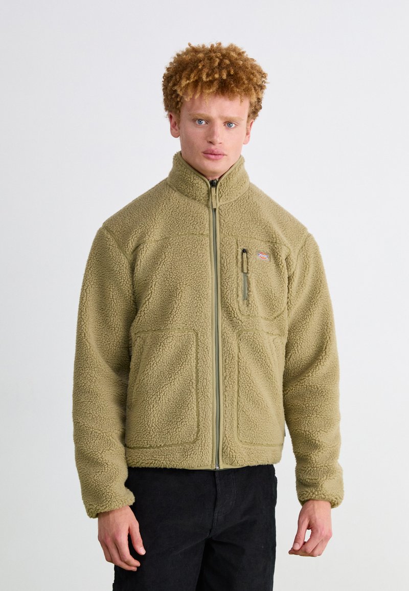 Brown fleece jacket with high collar, front zipper, and two large front pockets. Features a small logo on the upper left side.