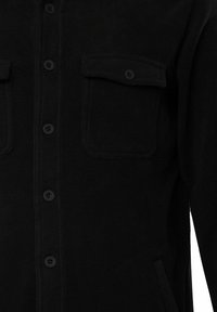 Camisa de forro negro con cierre de botones en la parte delantera, dos bolsillos en el pecho y una textura suave. Los botones también son negros para un aspecto uniforme.