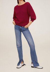 Burgundowy sweter dziany o fakturze z bufiastymi rękawami, zestawiony z jasnoniebieskimi, rozkloszowanymi dżinsami z bocznymi rozcięciami oraz białymi loafersami.