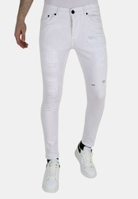 Witte skinny jeans met gescheurde details, voorzien van scheuren en rafelige accenten. Gecombineerd met witte sneakers en een aansluitend topje.