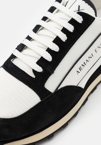 Baskets en suède noir et toile blanche avec lacets plats, semelle en caoutchouc et détail de logo subtil sur le côté. Le design texturé améliore l'adhérence.