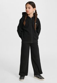 Czarna bluza z kapturem na zamek, luźny krój, z małym logo; w zestawie z pasującymi czarnymi dresami. Teksturowany materiał, styl casual.