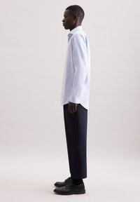 Lichtblauw gestreepte blouse met lange mouwen en button-down kraag, gedragen met op maat gemaakte marineblauwe broeken en zwarte schoenen. Soepele stof en een ontspannen pasvorm.