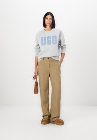Light gray sweatshirt with blue "UGG" logo, paired with beige wide-leg trousers, brown platform shoes, and a small brown handbag.