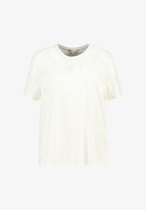 T-shirt blanc à manches courtes en tissu doux, présentant un motif floral en tissu texturé blanc sur l'épaule gauche. Encolure ronde.