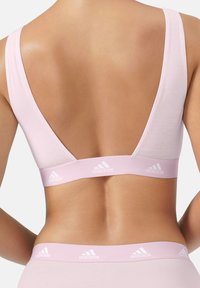 Ljust rosa sportbh med en bred rygg, som har en låg V-form. Den hållbara bandet har en vit Adidas-logotyp. Mjuk, slät tygkänsla.