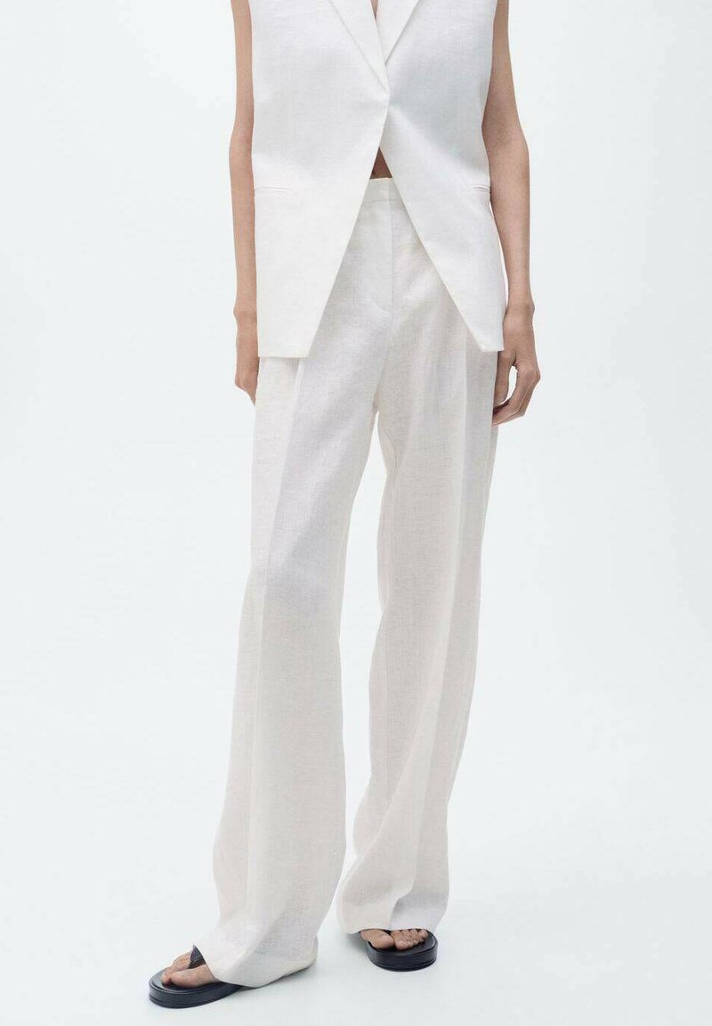 Vit linne ärmlös blazer och vida byxor, med en mjuk textur och minimalistisk design. Svarta platta sandaler fulländar outfiten.