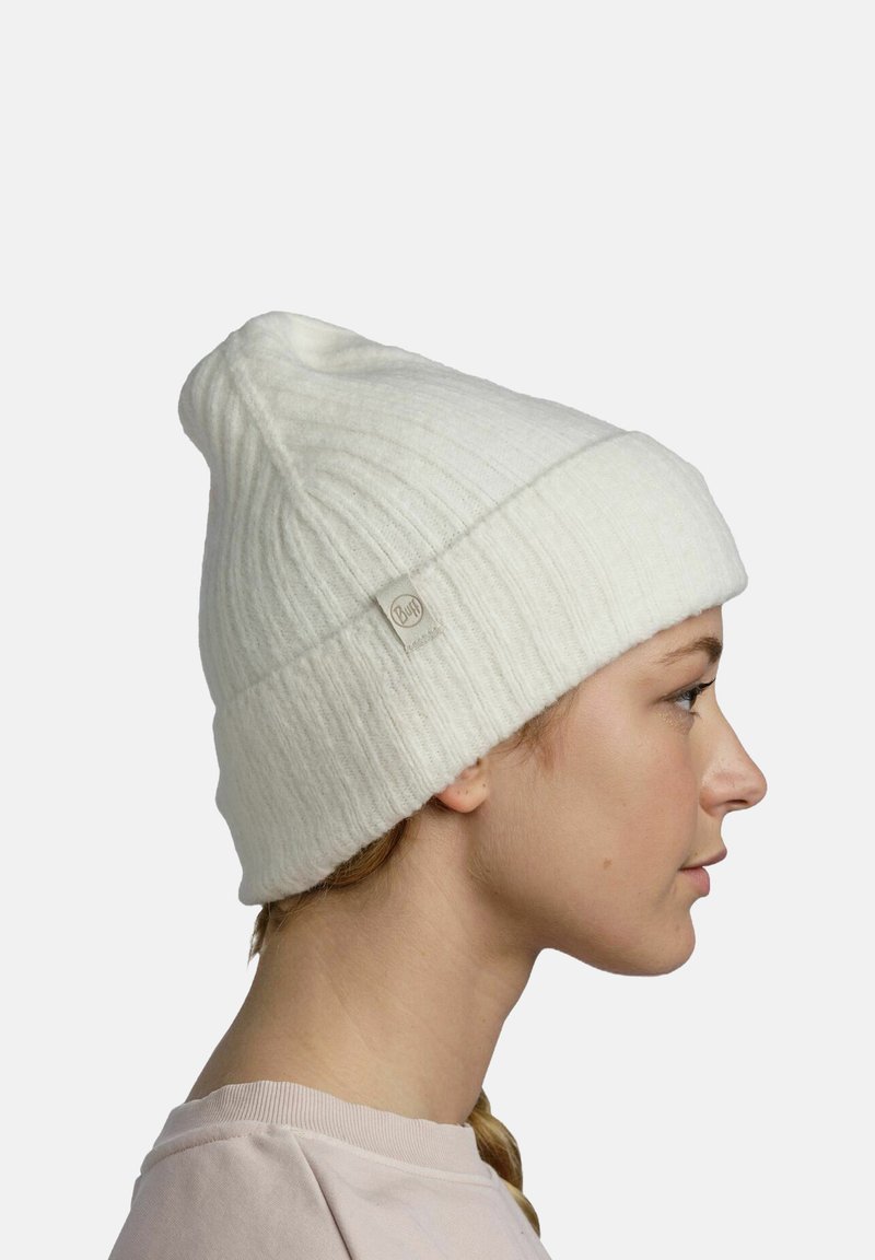 White knitted beanie with a ribbed pattern and a folded cuff. Features a small fabric tag on the side. Soft texture, conical shape.