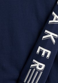 Marineblaues Sweatshirt mit auffälliger weißer Schrift entlang des Ärmels, weichem Material und klassischem Rundhalsausschnitt.