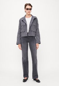 Grå cropped jakke med to frontlommer, kombinert med tettsittende grå jeans. Modellen har på seg en hvit topp og mørke solbriller. Glatt stoffstruktur.