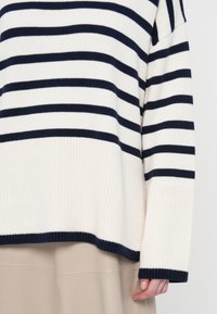 Maglione a collo alto lavorato a maglia con righe orizzontali crema e blu navy, con texture a costine e design ampio con maniche lunghe.