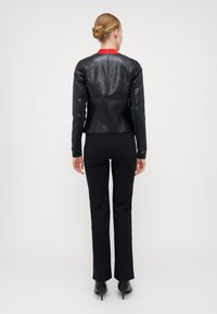 Veste en cuir noir avec un col rouge, coupe ajustée, manches longues et texture lisse, associée à un pantalon noir ajusté et des talons aiguilles.